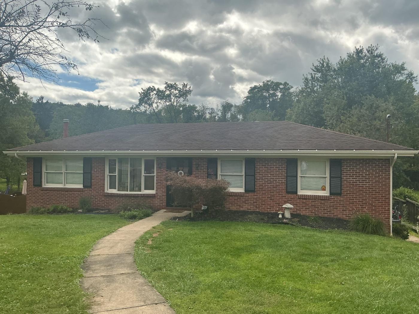 Single-story brick ranch home with gray roof, landscaped front yard and concrete walkway