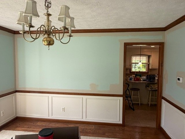 Formal dining room with light blue walls, white wainscoting, brass chandelier, and hardwood floors