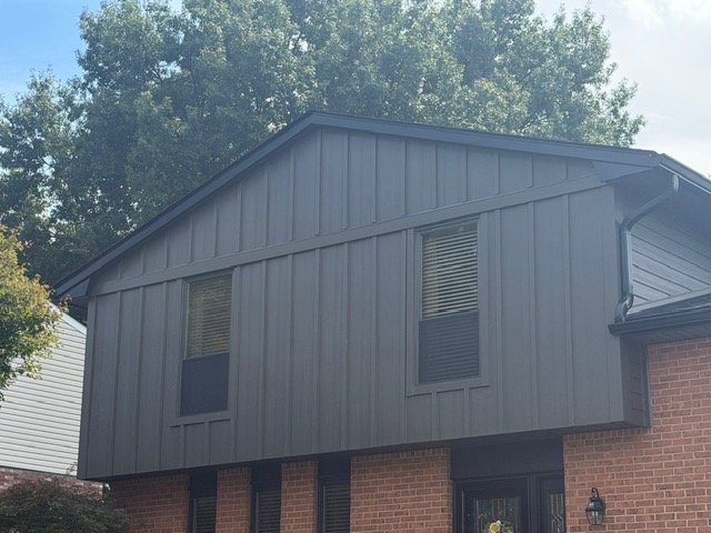 Modern dark metal siding addition on brick residential home with large windows