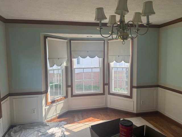 Bright sunlit room with bay windows, white wainscoting, mint green walls, and chandelier