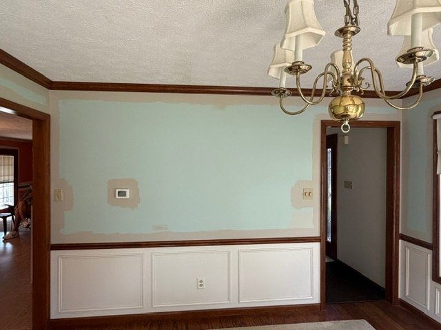 Dining room with light blue walls, white wainscoting, dark wood trim, brass chandelier, and hardwood floors