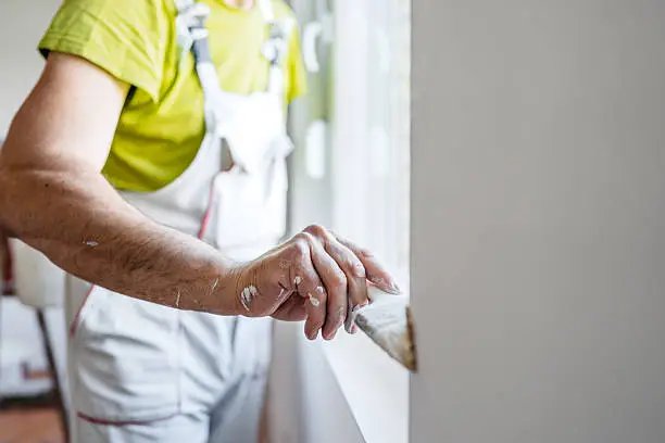 Worker in yellow shirt applying white paint or coating to wall with brush