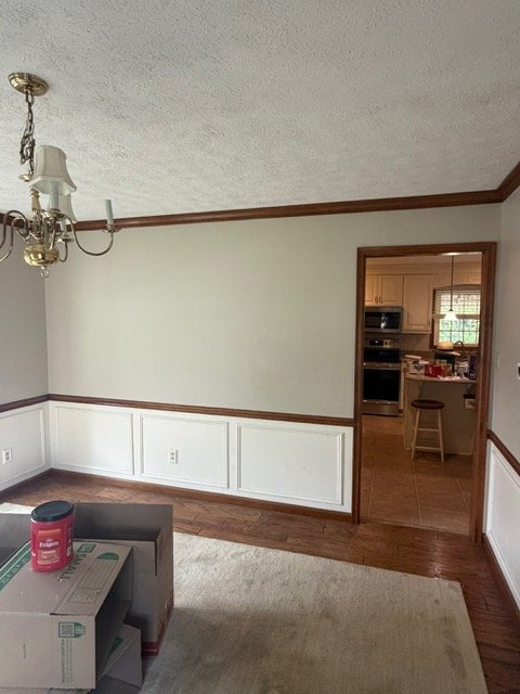 Empty dining room with white wainscoting, wood trim, chandelier, and hardwood floors
