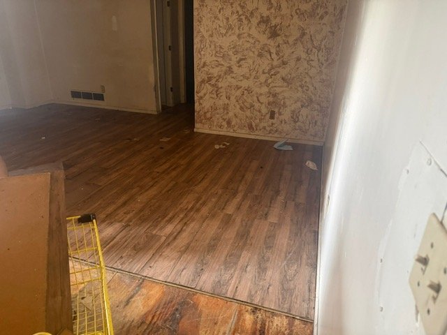 Empty room with wood laminate flooring and cork-textured wallpaper under renovation