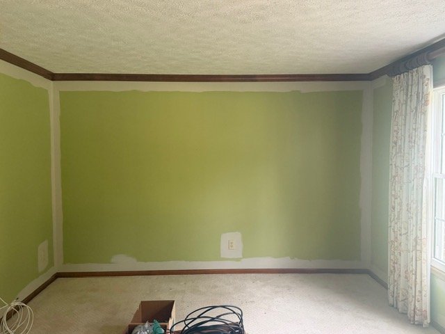Empty room with lime green walls, white trim, dark wood ceiling beams, and patterned curtains